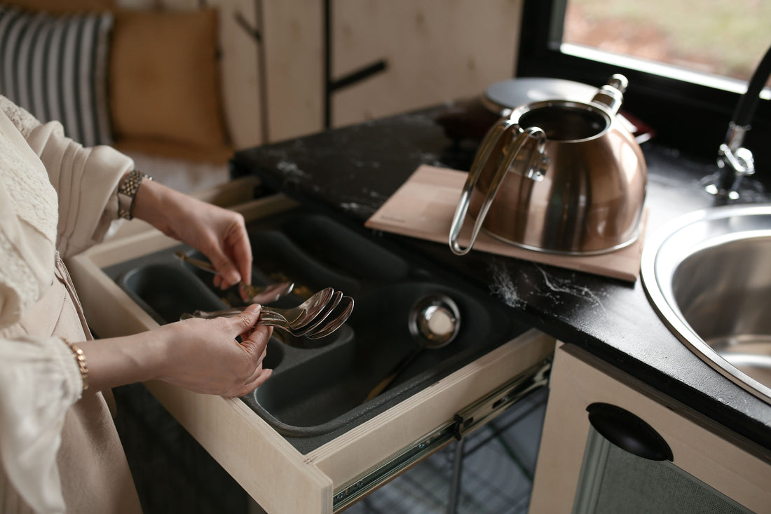 Woman organizing spoons in a kitchen drawer organizer next to a copper kettle.