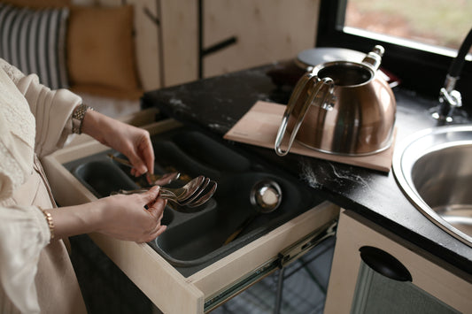 Woman organizing spoons in a kitchen drawer organizer next to a copper kettle.